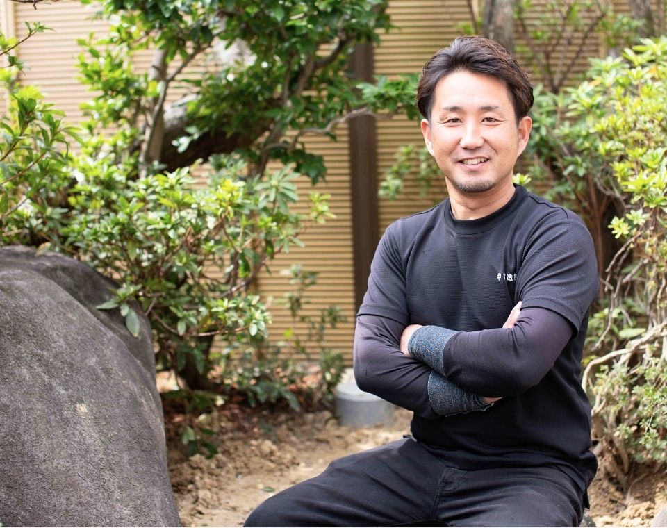 庭の手入れを行う職人が庭先で腕を組んで座っている様子