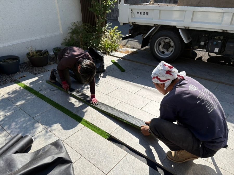 駐車場のスリット部分に人工芝を施工し、統一感のある仕上がりを目指している作業中の写真